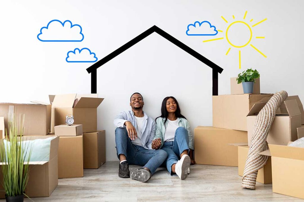 A young couple receives house keys inside an empty living room with moving boxes nearby.