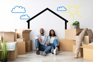 A young couple receives house keys inside an empty living room with moving boxes nearby.