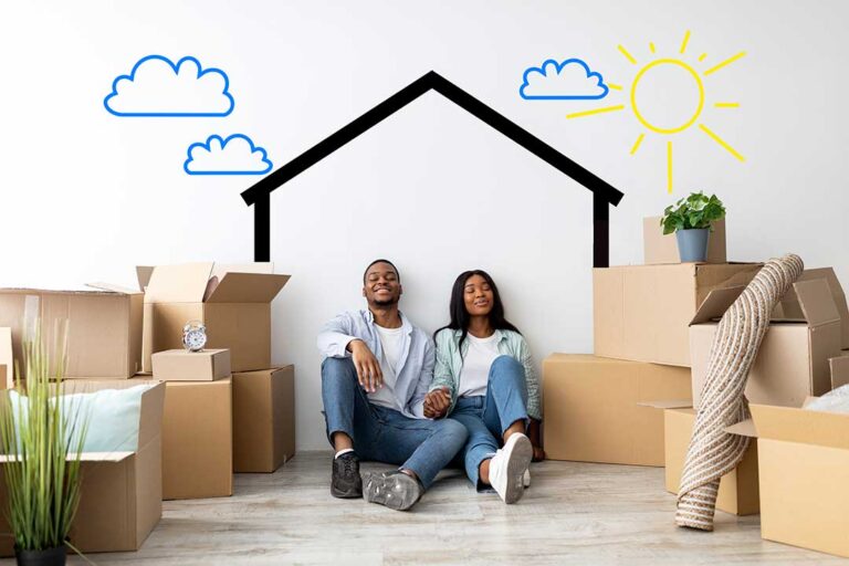 A young couple receives house keys inside an empty living room with moving boxes nearby.
