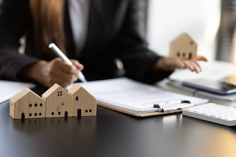 A couple reviews home purchase documents with a pen and calculator at a kitchen table.